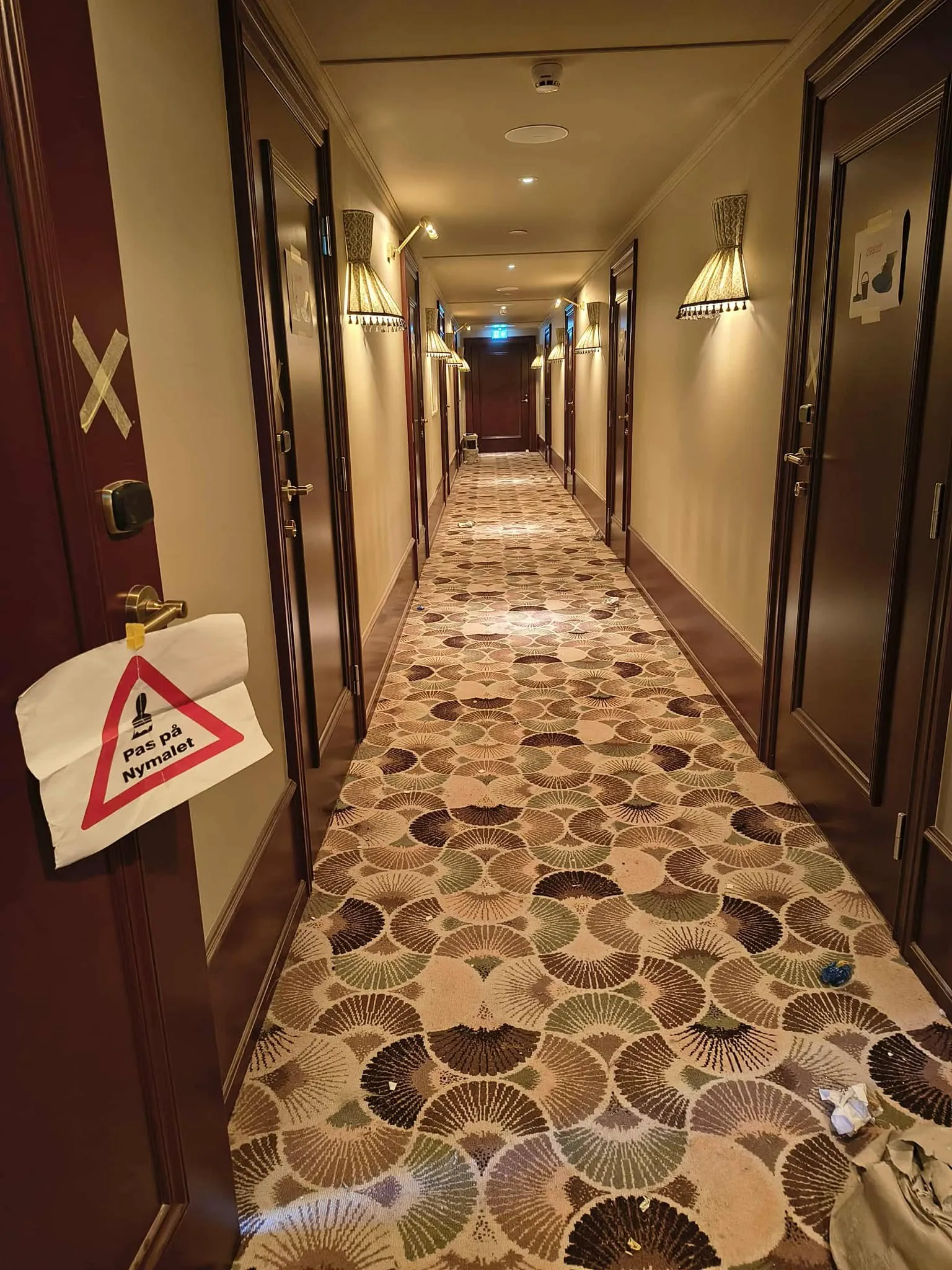 Langt hotelgang med døråbninger og advarselsmærke
